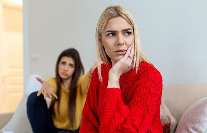 Woman in a red sweater looks upset, while another gestures in the background. Babysitter conflict depicted. Woman in a red sweater looks upset, while another gestures in the background. Babysitter conflict depicted.