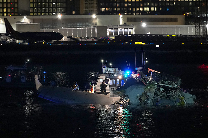 Boat crews inspect wreckage in water at night after plane crash near DC.