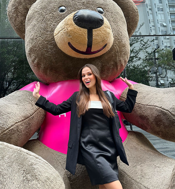 Woman posing happily with large teddy bear on street, relevant to seat swap lawsuit news.