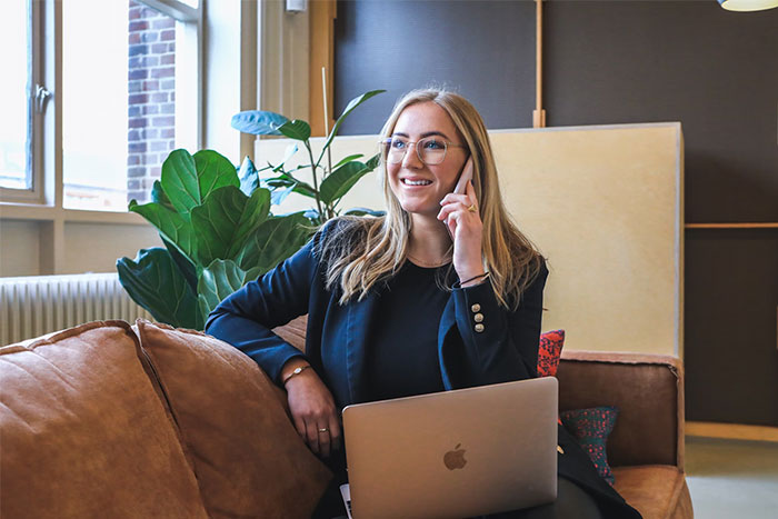 A woman talking on the phone with a laptop on her lap, possibly discussing red flags in potential employees.