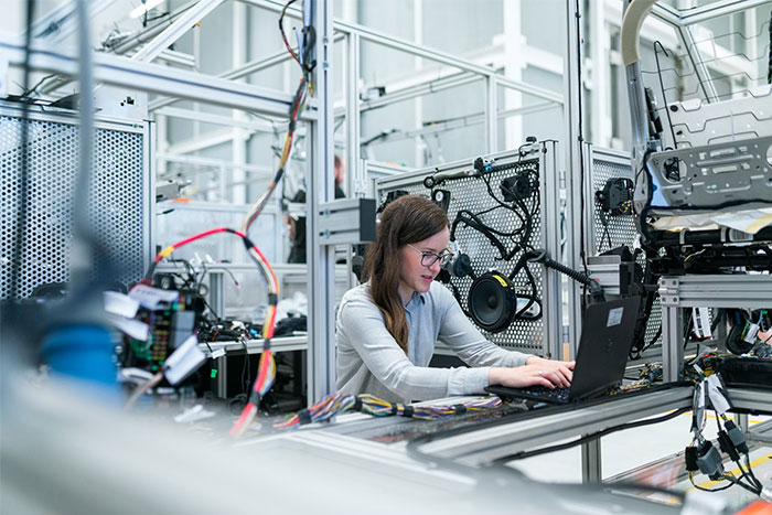 A woman working on a laptop surrounded by industrial equipment, exemplifying recruitment red flags in a technical setting.