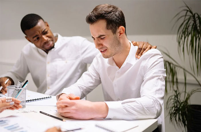Two men in white shirts, one comforting the other, possibly discussing red flags in potential employees.