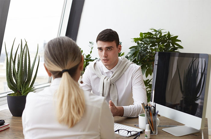 Man in a job interview with recruiter, discussing potential employee red flags; plants and computer in the background.