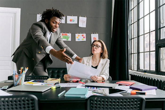 Recruiter discussing red flags with potential employee at a desk filled with colorful documents.