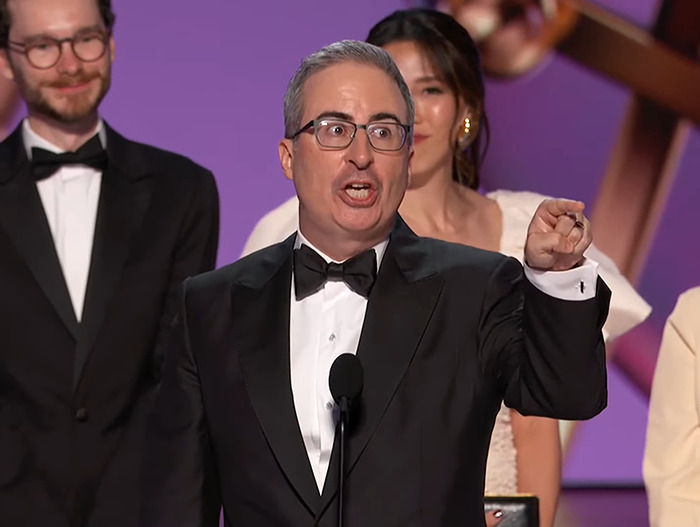 John Oliver in a tuxedo speaking enthusiastically on stage at an awards show, capturing an awkward moment in 2024.