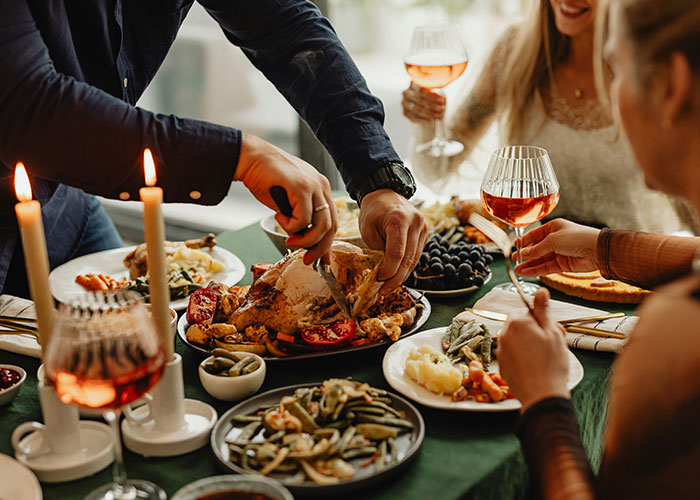 Dinner table with people enjoying a meal, featuring a carved turkey, wine glasses, and various side dishes.