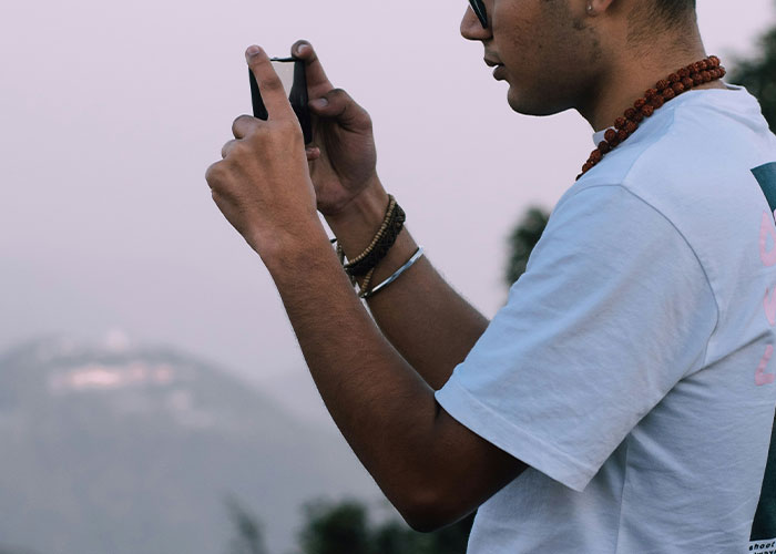 Person wearing a white t-shirt and necklaces, taking a photo in a natural setting, illustrating unusual human behavior.