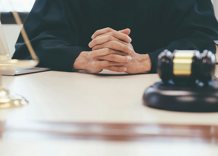 Hands clasped on courtroom desk beside gavel, symbolizing strange human behavior in legal settings.