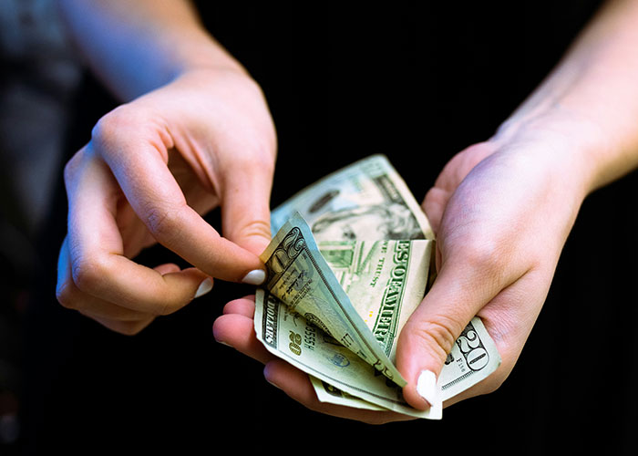 Hands holding and counting U.S. dollars, illustrating strange human behavior and money handling.
