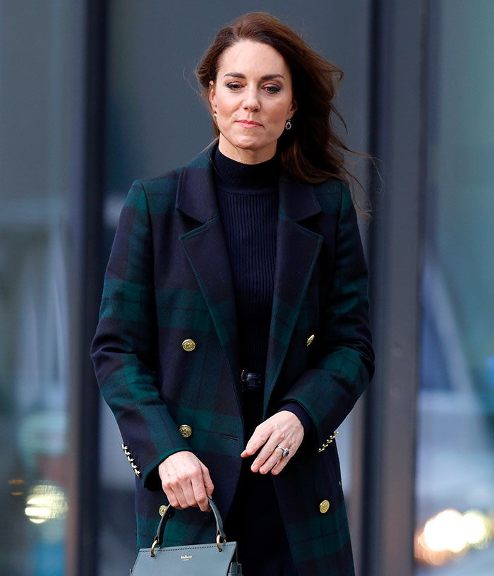 Woman wearing a ring and green coat, holding a handbag, sparking engagement ring mystery theories.