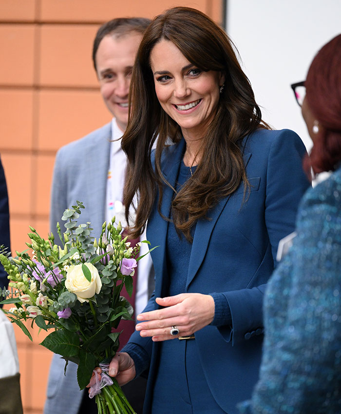 Woman in blue suit holding flowers, wearing an engagement ring.