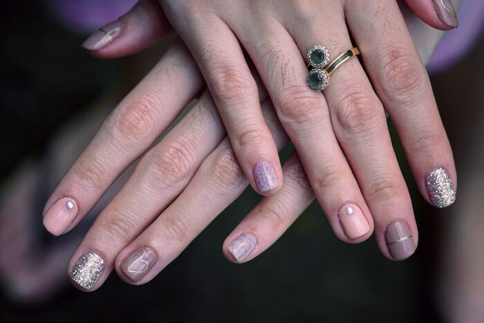 Hands displaying diverse nail art styles with glitter and geometric designs, showcasing current trends.