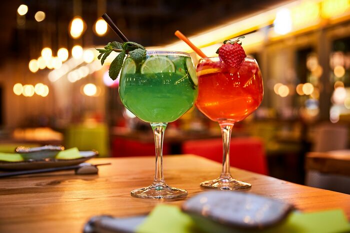 Two colorful cocktails on a wooden table in a trendy restaurant setting, highlighting current dining trends.