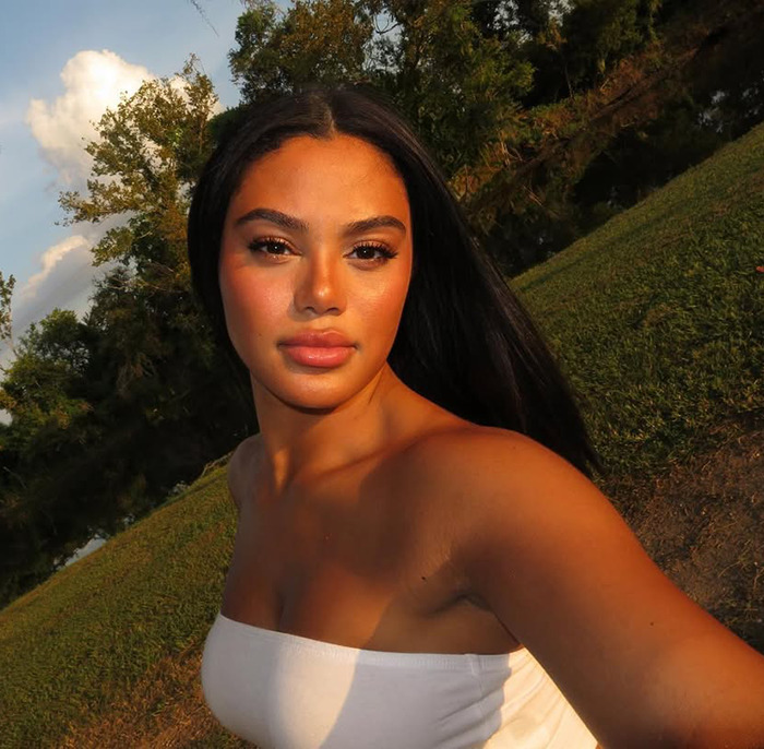 Kaya Odom outdoors with glowing skin surrounded by trees and a pond.