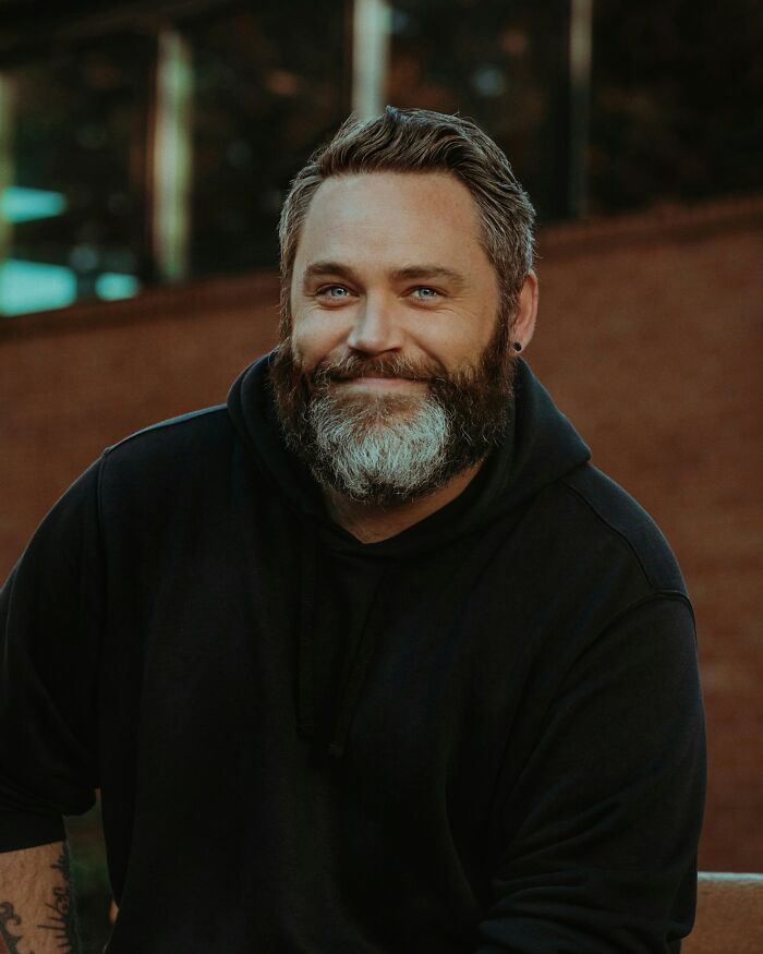 Bearded man in a black hoodie smiling, representing things men do that attract women.