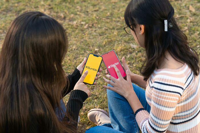 Two women sitting outdoors, holding phones with Bumble and Tinder apps, illustrating false advertisements theme.