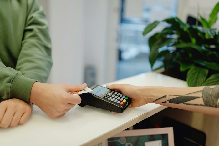 Person paying with a credit card at a store counter, highlighting consumer transactions and advertisements.