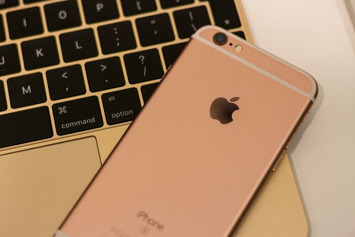 Rose gold iPhone placed on a gold laptop keyboard, symbolizing modern false advertising trends.