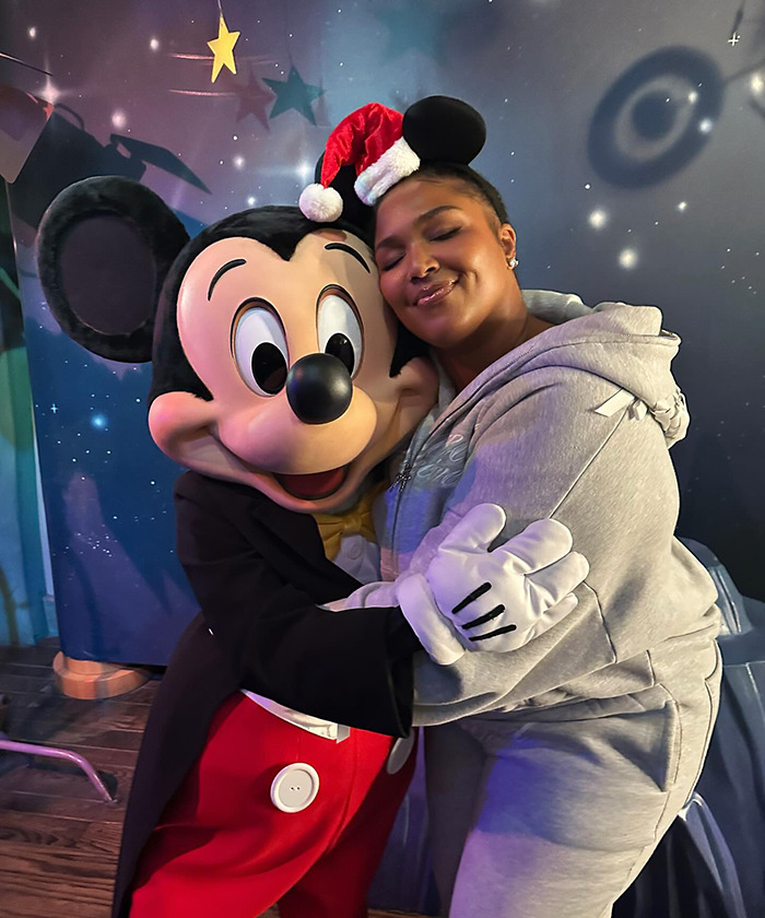 Lizzo in gray tracksuit hugging Mickey Mouse at a theme park, smiling and celebrating. Lizzo in gray tracksuit hugging Mickey Mouse at a theme park, smiling and celebrating.