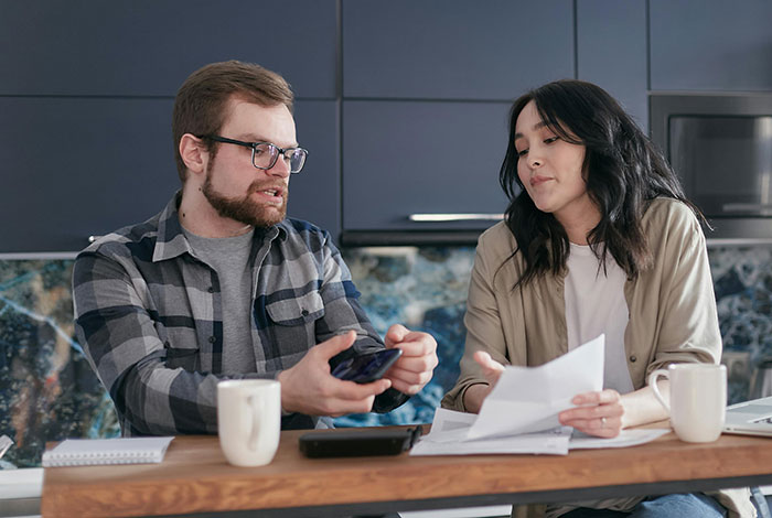 Man and woman discussing papers and phone over coffee at the kitchen table, related to infidelity accusations. Man and woman discussing papers and phone over coffee at the kitchen table, related to infidelity accusations.