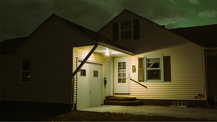 Night view of a dimly lit house exterior, front porch light on, suggesting a cautious home defense stance.