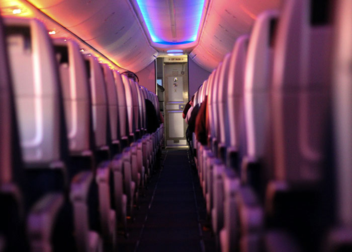 Airplane aisle view at night with seats illuminated by soft purple and orange lights. Airplane aisle view at night with seats illuminated by soft purple and orange lights.