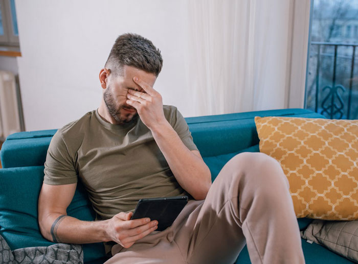 Man looking upset while sitting on a couch, holding a phone, symbolizing discovery of cheating.