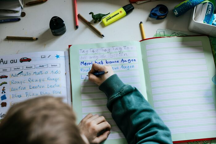 Child learning in a different country, writing in a notebook with colorful school supplies nearby.