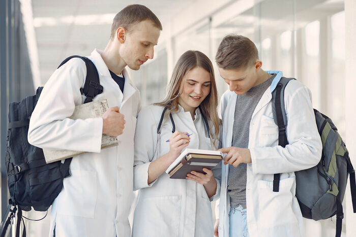 Group of medical professionals collaborating in a hallway, wearing lab coats and backpacks, discussing high-paying remote jobs.