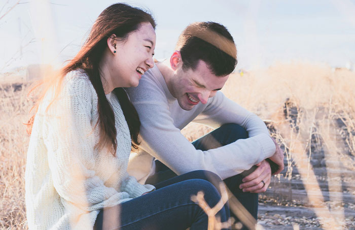 A man and woman laughing together in a sunny outdoor setting.