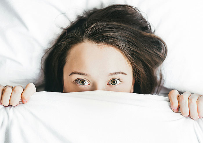 Woman hiding under a blanket, expressing curiosity about NSFW questions.
