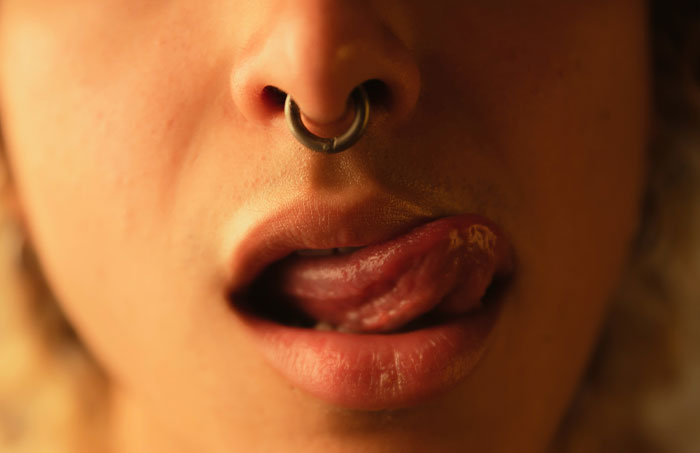 Close-up of a person with a nose ring, tongue out, highlighting NSFW questions theme.