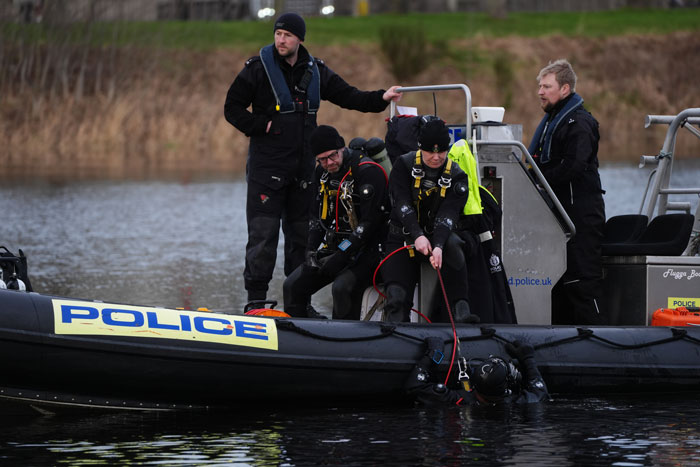 Police divers search a river for missing sisters, standing on a police boat.