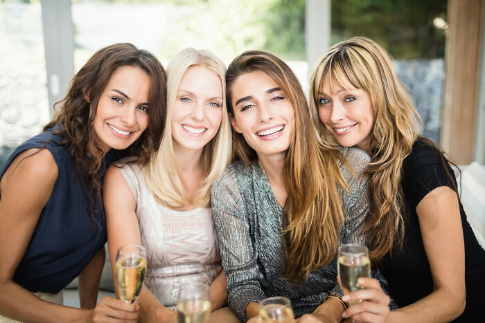 Four women smiling and holding champagne glasses, capturing a joyful moment among friends at a birthday celebration.