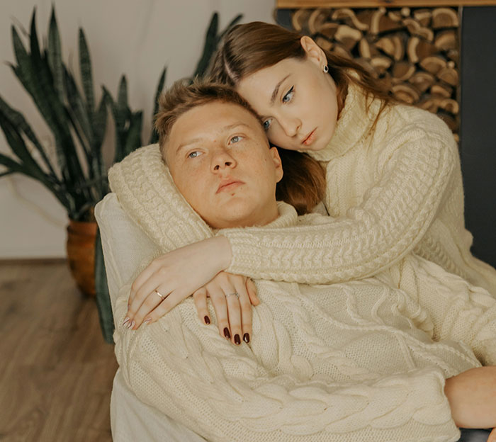 Couple in cozy sweaters embracing on a couch, sharing a touching moment in a warm setting.