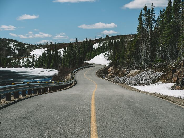 Winding road through snowy landscape in the worst country ever visited, bordered by trees and a clear sky.