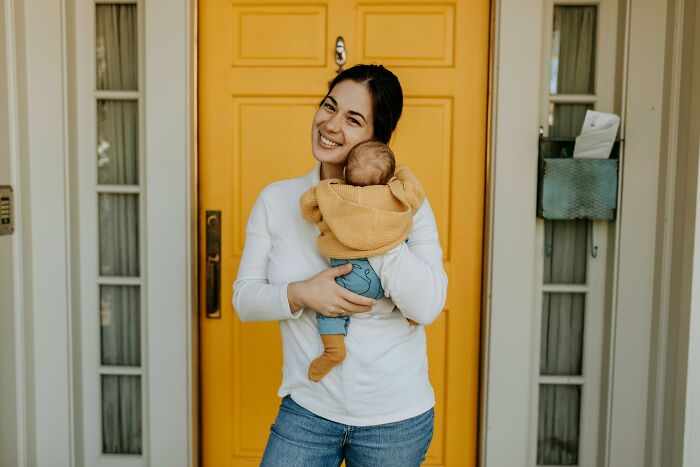 Woman smiling at door holding a baby in front of a yellow door.