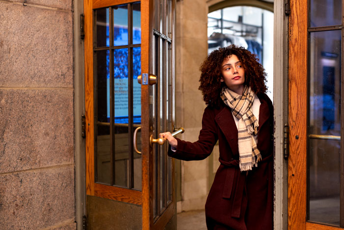 Woman opening a door in a building entrance, wearing a scarf and coat, appearing concerned about blocked access.