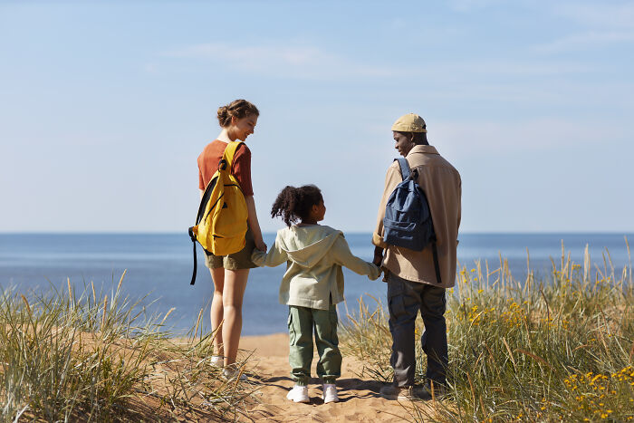 Family with backpacks walking on a beach path, symbolizing middle class lifestyle challenges.