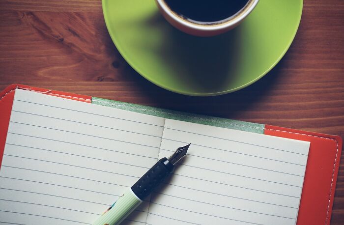 Open notebook with a pen and a cup of coffee on a wooden table, symbolizing budgeting ideas.