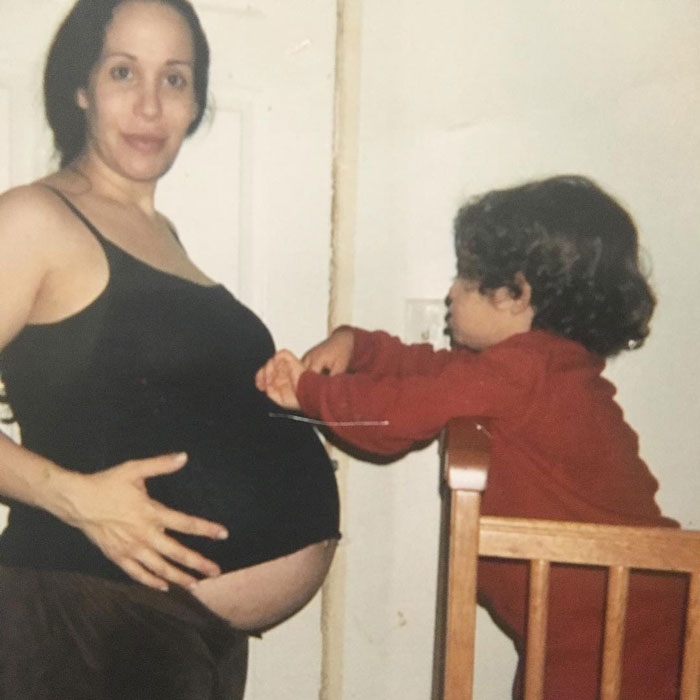 Nadya Suleman with child, showing her pregnant belly, wearing a black tank top, in a warm home setting. Nadya Suleman with child, showing her pregnant belly, wearing a black tank top, in a warm home setting.