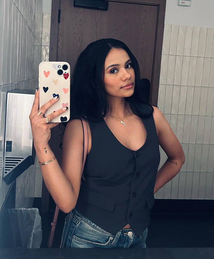 Woman in a gray vest takes a mirror selfie, reflecting on dating profiles and modern relationships.