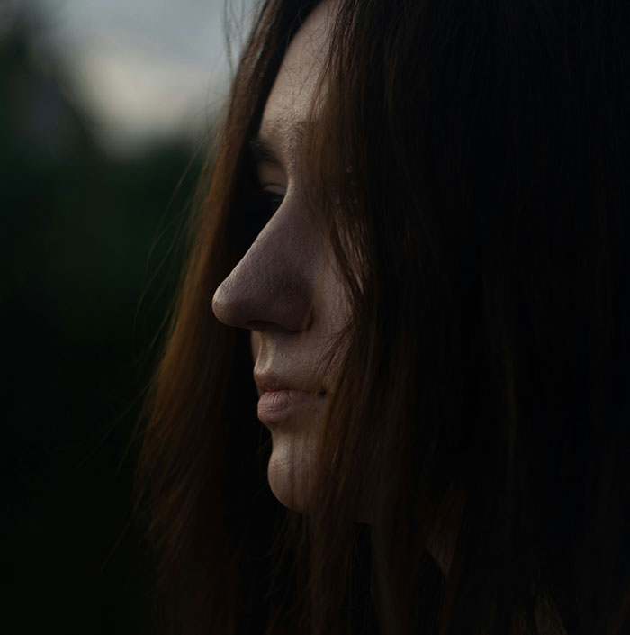 Woman's side profile in a dark setting, capturing a contemplative mood.