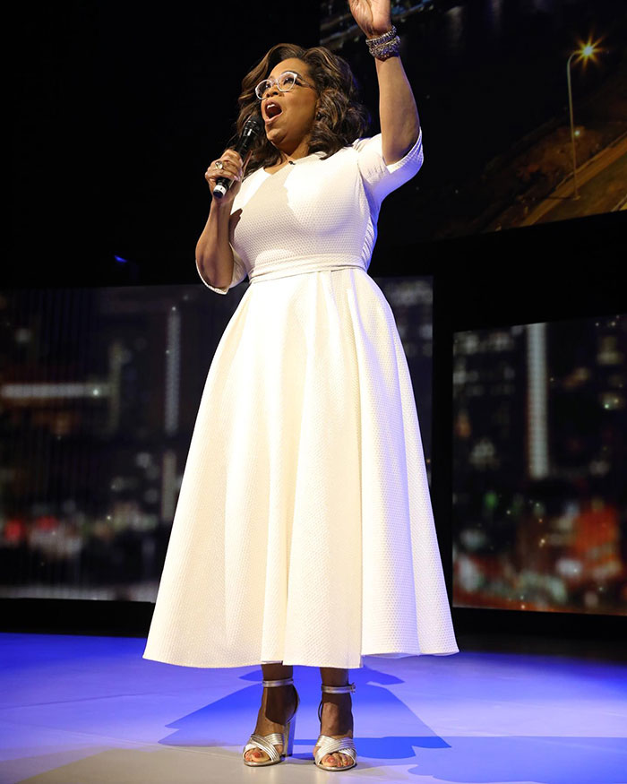 A woman on stage, wearing a white dress and holding a microphone, speaking passionately about thin people and Ozempic. A woman on stage, wearing a white dress and holding a microphone, speaking passionately about thin people and Ozempic.
