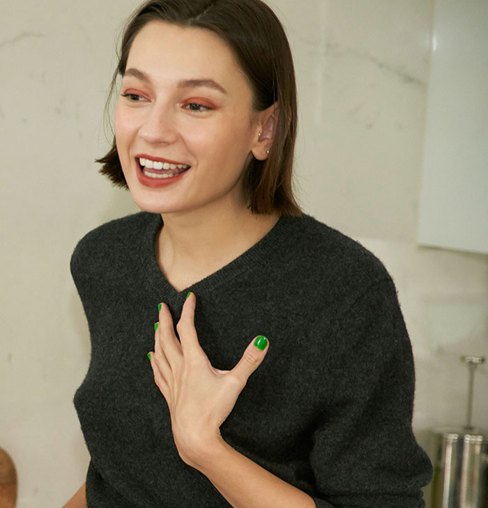 Young woman wearing a dark sweater, hand on chest, smiling in a candid moment. Young woman wearing a dark sweater, hand on chest, smiling in a candid moment.