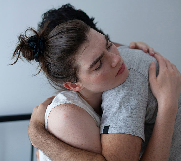 A woman with a solemn expression receiving a comforting hug, conveying emotional support. A woman with a solemn expression receiving a comforting hug, conveying emotional support.