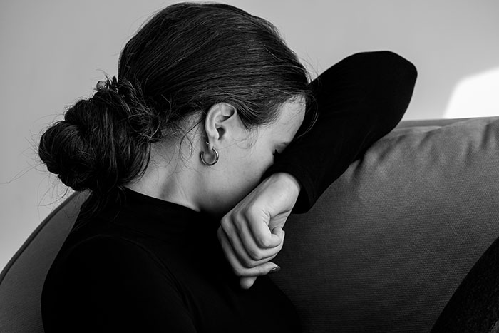 A woman in distress, sitting on a couch, covering her face with her arm, showing emotion related to a miscarriage. A woman in distress, sitting on a couch, covering her face with her arm, showing emotion related to a miscarriage.