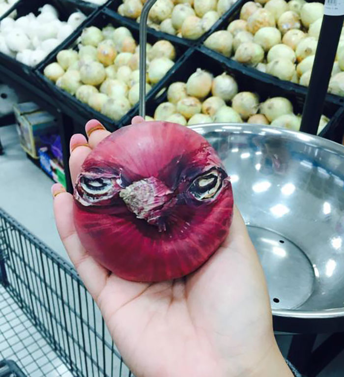 Hand holding a red onion with face-like marks, illustrating pareidolia in a grocery store setting.