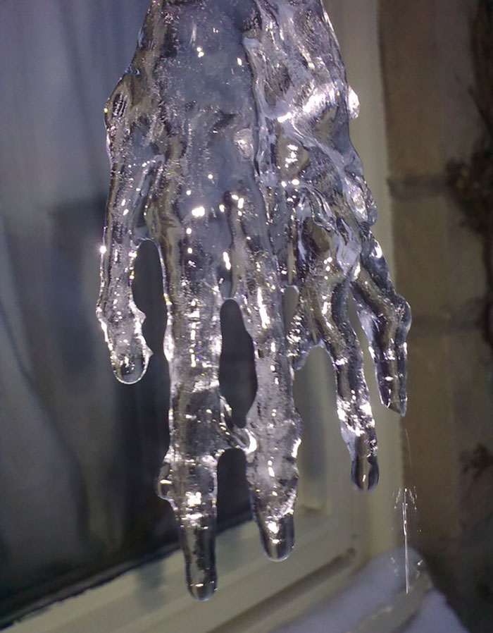 Icicle resembling a hand, capturing a common pareidolia phenomenon against a window backdrop.