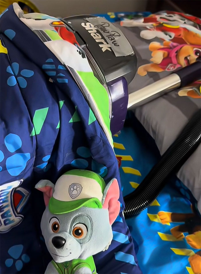 Mom vacuuming cartoon-themed bedspread; cleaning dirt thought to be on son's floor.